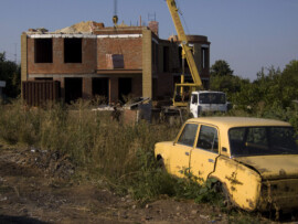 Hinten entsteht ein neues Gebäude, vorne verrostet ein altes Auto Baustelle und Schrottauto
